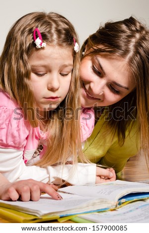 Elder sister teaches to read younger one at home on floor