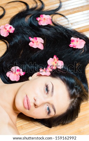Beautiful girl face & pink flowers, perfect skin and lips looking at camera