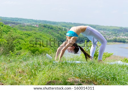 Happy young woman doing yoga on green river bank in summer outdoors