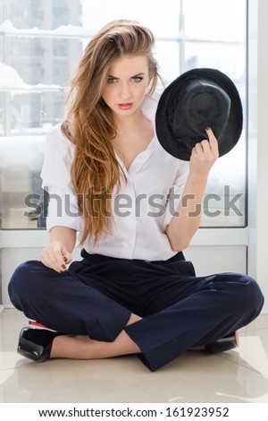 Young business woman looking bossy wearing man\'s shirt holding stylish hat in office