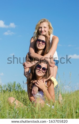 Three happy girls embracing & happy smiling & looking at camera against blue sky on summer outdoors background