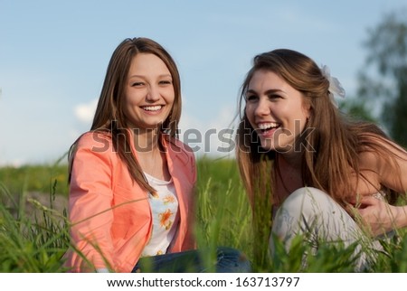 Two Teen Girl Friends Laughing  in green grass & looking at camera on summer day