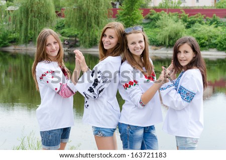 Four happy young women girls friends posing in handmade blouses and holding hands happy smiling & looking at camera outdoors