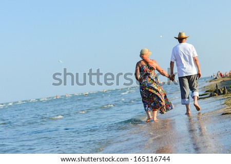 Happy mature couple walking at seashore on sandy beach and embracing on summer sea outdoors background
