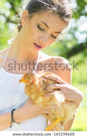 Happy young woman taking care of chicken on green summer outdoors background