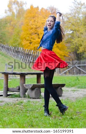 Young happy woman n short red skirt spinning around on autumn day outdoors background