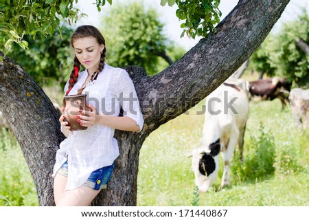 Young happy woman drinking fresh milk near cows in countryside