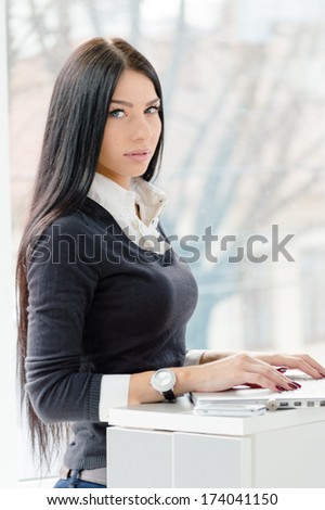 Portrait of a happy young business woman using notebook PC relaxing near office window