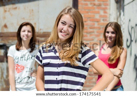 Three happy teenage friends smiling at urban background on summer day