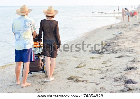 Young happy family with baby stroller walking on sandy beach