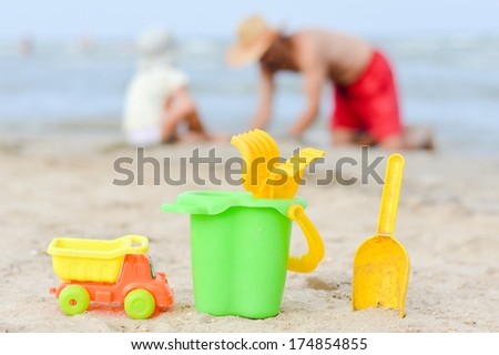 Father and son playing on sandy beach toys closer to viewer