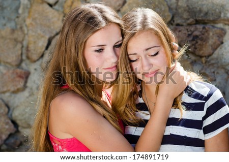 Teenage girl comforting crying friend with warm hug on stone rock wall background