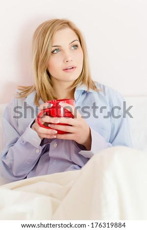 looking up beautiful happy smiling young woman in bed holding cup of hot drink or water