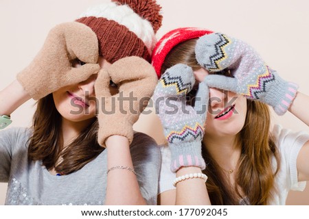 Beautiful happy smiling young women girl friends wearing knitted gloves and hat showing binoculars