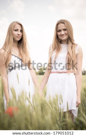 Two young women happy smiling blond girl friends walking in green field & looking at camera on summer outdoors background portrait