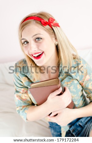 book lover: beautiful blonde pinup young woman happy smiling girl with red lipstick looking at camera & holding book or bible