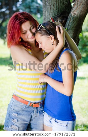 Two happy teenage girls sharing secret on summer green outdoors background