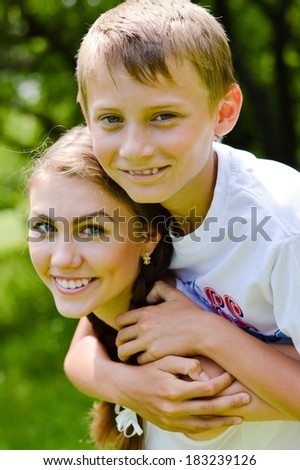 Teenage sister and little brother hugging outdoors on summer day green background