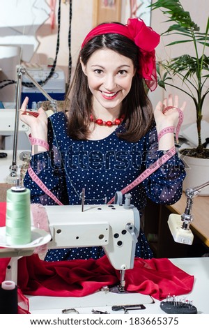 Funny young pinup pretty woman in polka dot dress with sewing machine and measuring tape happy smiling & looking at camera portrait