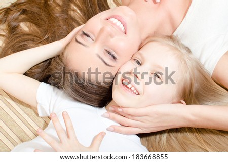 Beautiful attractive woman with child girl closeup lying face to face happy smiling & looking at camera portrait