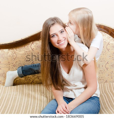 young woman sitting on a couch and the girl child whispers something in her ear