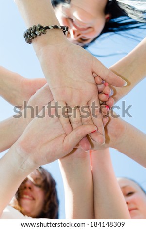 Pile of friends hands symbol of teamwork with blue sky on the background closeup