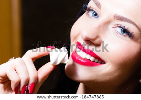 closeup portrait on seductive charming beautiful young woman with blue eyes, red lips & hand with red nails holding candy