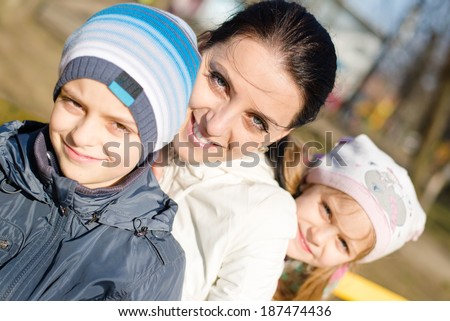 3 people beautiful young mother with two children, son and daughter having fun happy smiling & looking at camera, closeup portrait on spring or autumn outdoors background