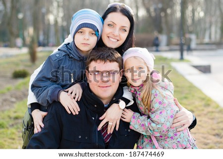 Happy family of 4 closeup portrait: Parents with two children hugging, happy smiling & looking at camera on the spring or autumn outdoors background closeup portrait