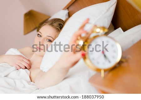 beautiful blond young business woman blue eyes girl touching alarm clock off wake up time looking at the camera smiling looking at camera