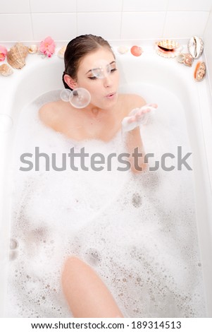 relaxing beautiful woman lying in a spa bath with foam and shell  having fun blowing soap bubbles portrait