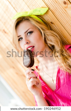 eating chocolate icecream pin up beautiful blond young woman with green eyes red lips in a pink shirt having fun relaxing and looking at camera closeup portrait picture