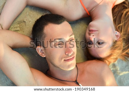closeup portrait of young beautiful couple in love looking at each other lying on sandy ground outdoors