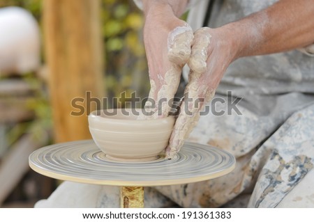 closeup image of craftsman hands making vase from fresh wet clay on pottery wheel