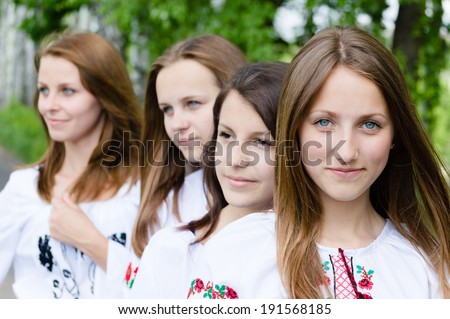 4 happy smiling young pretty women teenage girl friends standing in line & one looking at camera on green summer outdoors background closeup picture