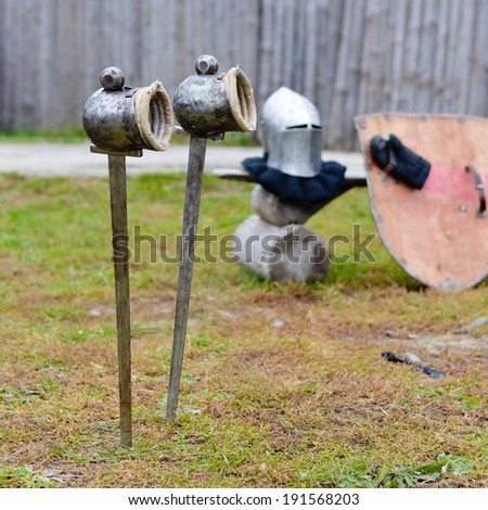 Two swords with gloves waiting in ground before festival knight battle with rustic temple wooden fence on the background