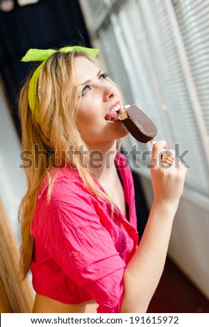 image of eating chocolate ice cream pin up beautiful blond young woman with green eyes red lips in a pink shirt having fun relaxing and looking out the sunny window closeup portrait