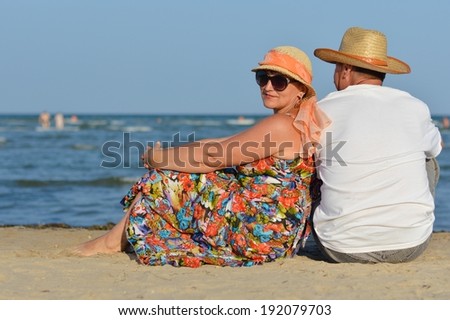 image of happy mature couple having fun relaxing sitting back to back at seashore on sandy beach summer sea outdoors background