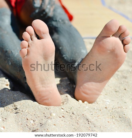 picture of closeup on man sitting on sandy ground beach applying mineral blue mud on knee