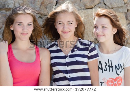 closeup image of 3 beautiful young women teen girl friends having fun happy smiling & looking at camera on natural stone summer outdoors background