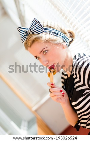 picture of closeup portrait on eating chocolate bar beautiful blond young woman sexy pinup girl with red lips having fun on the sun lighting window background