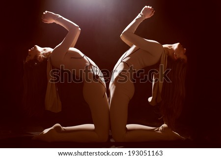 picture of praying 2 slim show girls pretty women showing theater performance in body suits on dark stage background with light from above