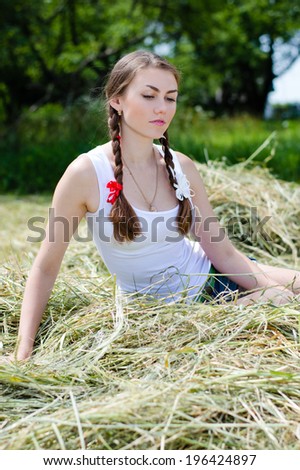 picture of beautiful young woman sensual girl with red & white ribbon in fair hair having fun sitting thoughtful on dry hay summer day outdoors background portrait