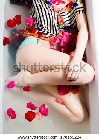 Image of beautiful sexy young woman legs in bath with rose flowers petal. Spa body care treatment.