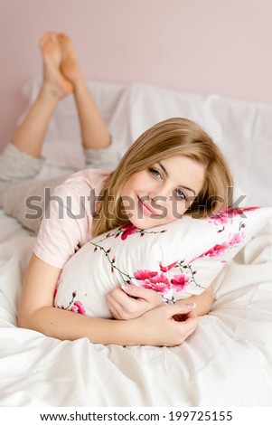 portrait of beautiful happy young blond woman romantic blue eyes girl having fun relaxing in bed with floral pillow in hand happy smiling & looking at camera on light copy space background picture