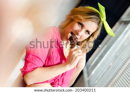 having fun cheerful beautiful young woman pretty blond pin up girl with red lips licking ice cream in chocolate glaze with lens flare looking into the camera closeup portrait image