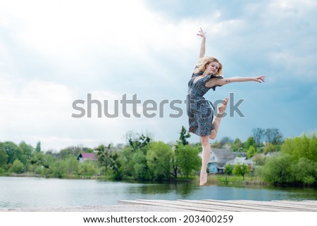 feeling high: portrait of beautiful blond dancing girl with falling sun lighting rays from blue sky at water lake or river on spring or summer nature green outdoors copy space background picture
