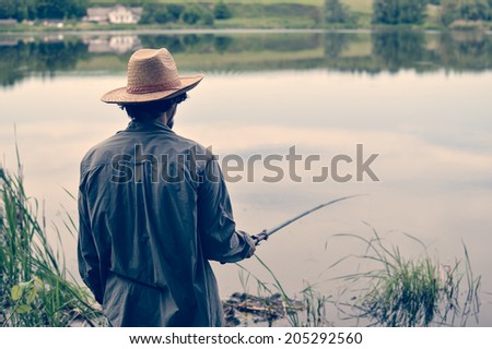 picture of man in straw hat having good time & fun fishing on river bank on peaceful summer day & water outdoors copy space background portrait
