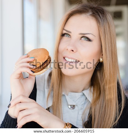 enjoying burger: eating delicious hamburger beautiful young woman cute blond girl having fun in restaurant or coffee shop happy smiling & looking at camera on copy space background closeup portrait