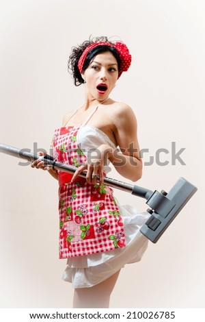 portrait of housewife attractive pin-up girl having fun showing surprise & excitement because the vacuum cleaner eats her mini dress, standing on light copy space background